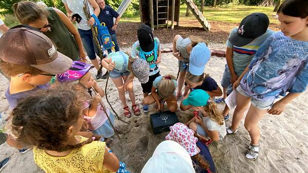 Themenbild: Kinder stehen rund um die Schatztruhe Themenbild: Kinder stehen rund um die Schatztruhe