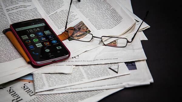 Themenbild: Auf einer Zeitung liegt eine Brille und ein Smartphone.