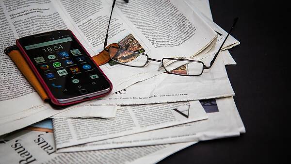 Themenbild: Auf einer Zeitung liegt eine Brille und ein Smartphone. Themenbild: Auf einer Zeitung liegt eine Brille und ein Smartphone.