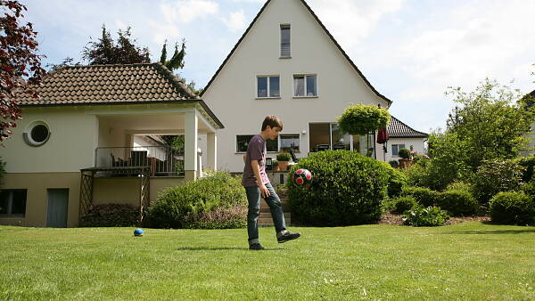 Themenbild: Haus mit Garten und Junge mit Fußball