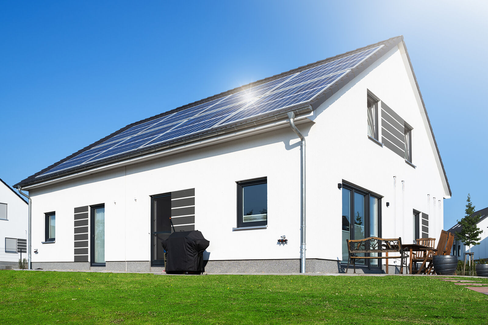 Ein weißes Haus mit Solarpanels auf dem Dach vor blauem Himmel, vor dem Haus ist ein grüner Rasen