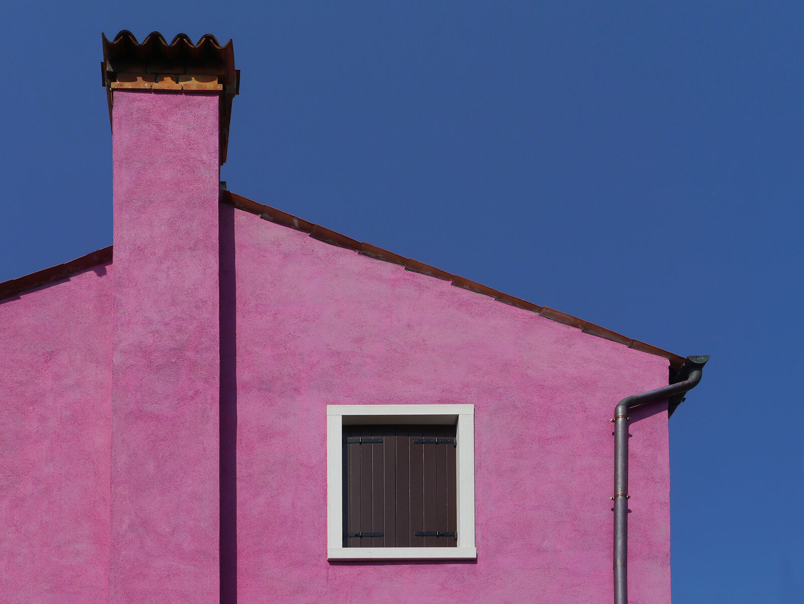 Ein rosafarbenes Haus vor blauem Himmel mit einem Fenster mit Sonnenschutz