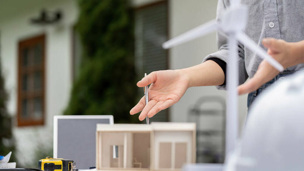 Eine Hand zeigt auf ein kleines Holzmodell eines Hauses