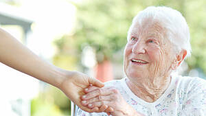 Eine weißhaarige alte Dame hält die Hand eines Betreuers.