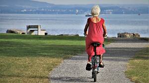 Seniorin im roten Kleid fährt auf einem Rad Richtung See