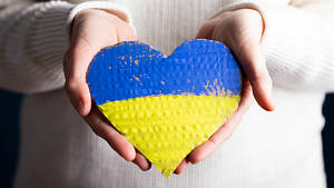 Ein blau-gelbes Herz aus Pappe wird dem Betrachter auf zwei Händen entgegengereicht