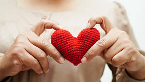 zwei Hände halten ein kleines rotes gehäkeltes Herz