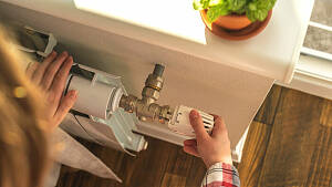 Eine Hand dreht am Thermostat eines Heizkörpers