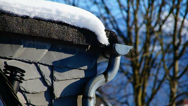 Themenbild: Dachrinne und Fallrohr an einem mit Schnee bedeckten Dach