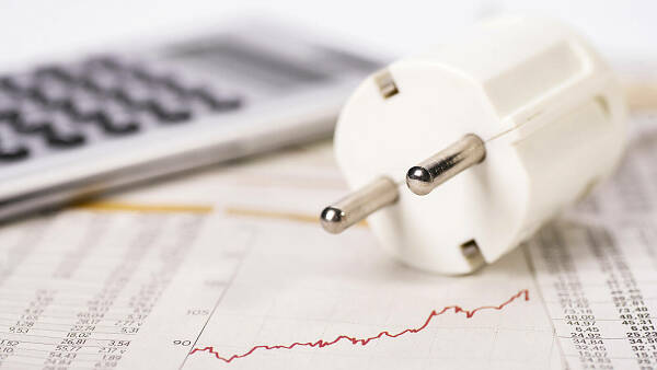Themenbild: Ein Stecker und ein Taschenrechner liegen auf einem Diagramm, das steigende Energiekosten symbolisiert.