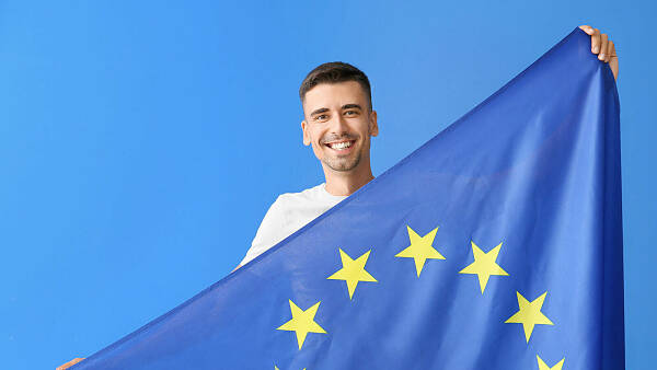 Themenbild: Junger Mann lächelnd mit Europaflagge