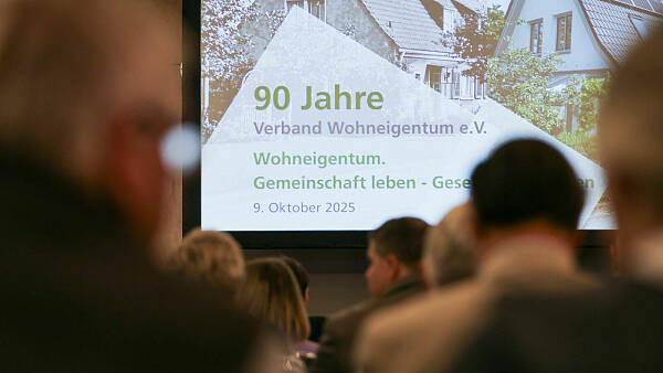 Themenbild: Blick von hinten in einen vollbesetzten Sall auf einen Beamer, Augschrift 90 Jahre Verband Wohneigentum Themenbild: Blick von hinten in einen vollbesetzten Sall auf einen Beamer, Augschrift 90 Jahre Verband Wohneigentum