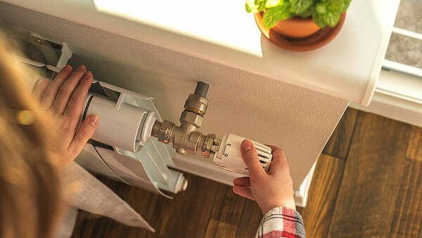Themenbild: Eine Hand dreht am Thermostat eines Heizkörpers