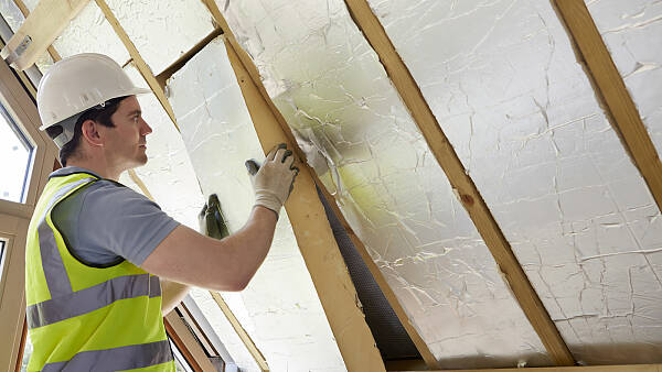 Themenbild: Bauarbeiter mit gelber Warnweste und Helm dämmt ein Dach von innen.