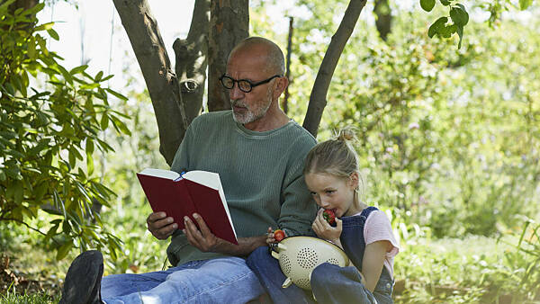Themenbild: älterer Mann liest Kind unter Baum vor