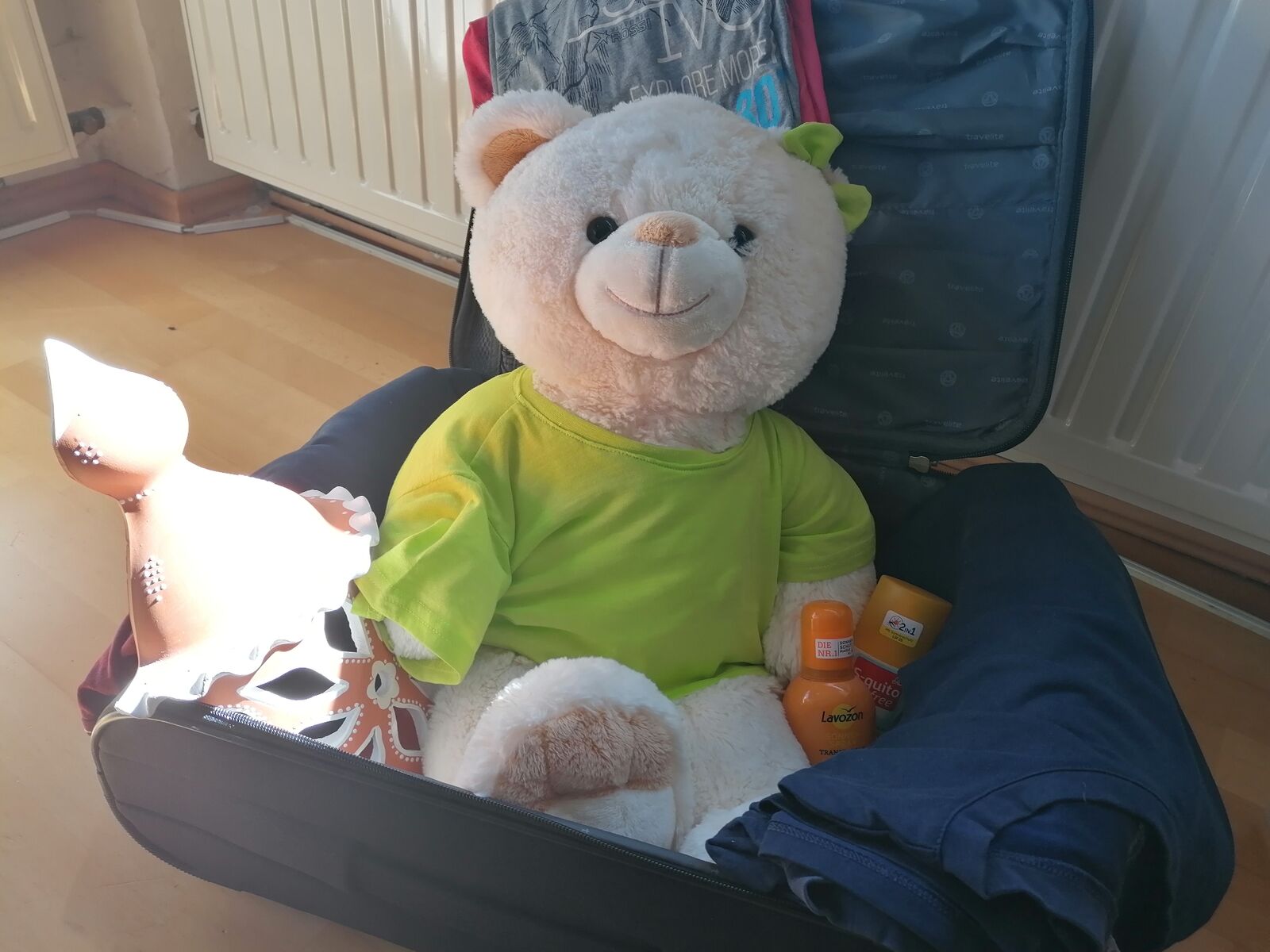 Maskottchen Bärbel sitzt in einem Koffer mit Urlaubsmitbringsel