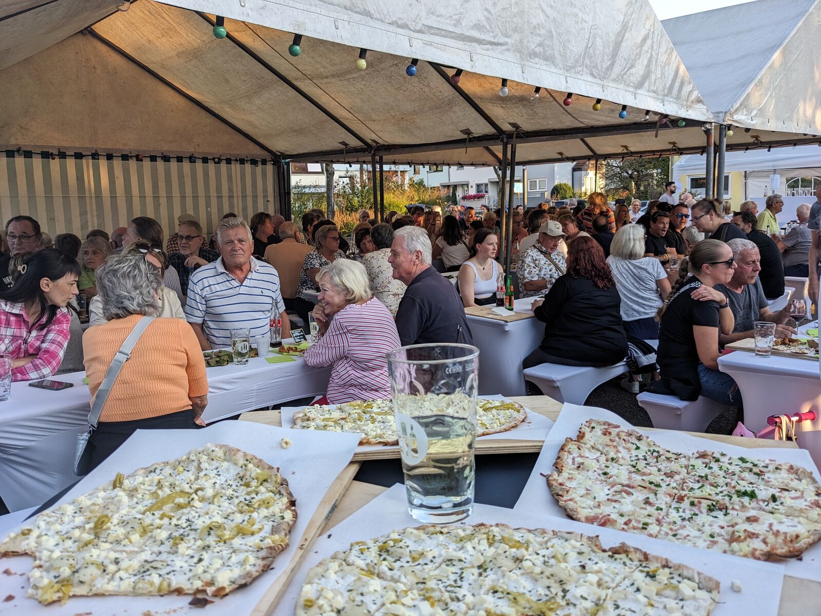 Besucher beim Weinfest, im Vordergrund Flammkuchen und Schoppenglas