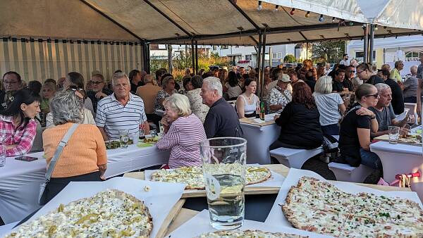 Themenbild: Besucher beim Weinfest, im Vordergrund Flammkuchen und Schoppenglas